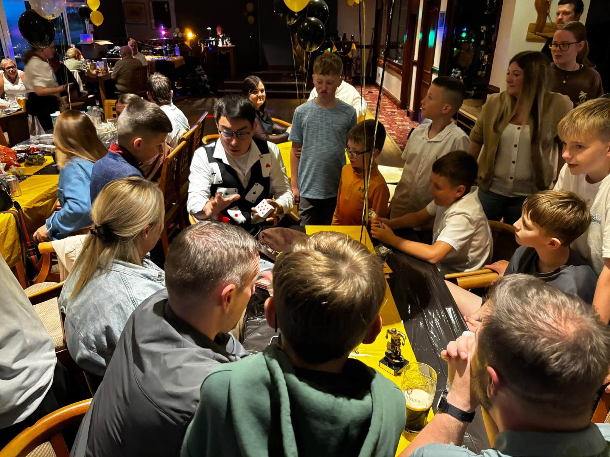 Magic Yin performing close-up magic for a large party crowd in Edinburgh, surrounded by adults and children